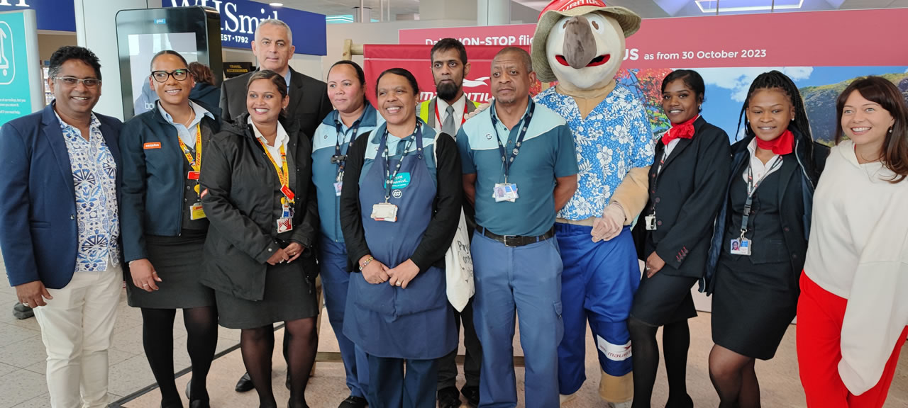 Michel Roy Luchmun (premier à gauche), Laurent Recoura (quatrième à gauche) et la chanteuse locale Anne Ga, en compagnie de la mascotte, le dodo, et des employés mauriciens travaillant à l’aéroport de Gatwick lundi après-midi. Soit peu avant le vol inaugural Gatwick-Maurice.